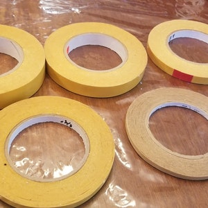 May include: Five rolls of yellow and brown tape. The tape is on a wooden surface.