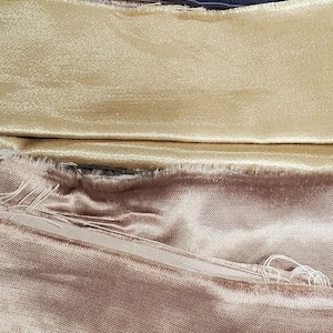 May include: A stack of fabric swatches in various colors, including dark green, navy blue, gold, beige, and red. The fabric is smooth and silky.