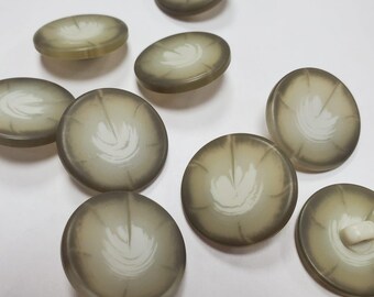 Peut inclure: Un ensemble de boutons ronds et translucides présentant un design dégradé passant d'un bord vert olive foncé à un centre plus clair et crémeux. Chaque bouton affiche un motif blanc en forme de feuille rayonnant du milieu vers le bord.