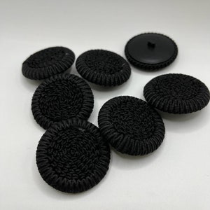 Peut inclure: Sept boutons noirs avec un motif en relief texturé. Les boutons sont ronds et ont un dos lisse et plat.