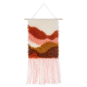 Op de afbeelding: Een rechthoekige wandhanger met een getextureerd, gelaagd ontwerp in crème, roest, roze, goud en bruin. Het kunstwerk is opgehangen aan een houten deuvel met een wit koord en heeft onderaan een franje van roze garen.