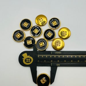 Peut inclure: Un groupe de dix boutons noirs et dor&eacute;s avec un motif carr&eacute; au centre. Les boutons mesurent environ 1,5 cm de diam&egrave;tre.