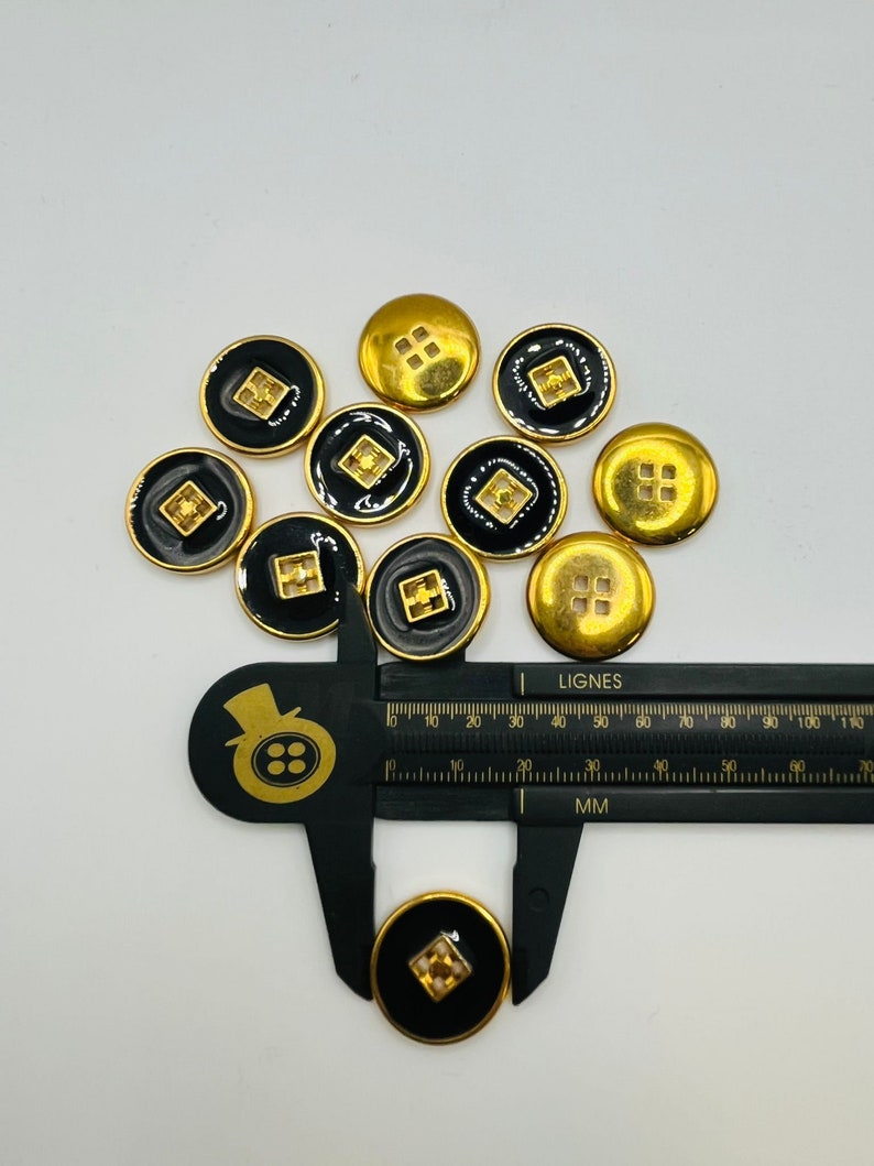 Peut inclure: Un groupe de dix boutons noirs et dor&eacute;s avec un motif carr&eacute; au centre. Les boutons mesurent environ 1,5 cm de diam&egrave;tre.