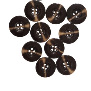 Peut inclure: Une collection de boutons marron foncé avec un effet marbré. Chaque bouton a quatre trous et un bord légèrement surélevé. Les boutons sont disposés sur un fond blanc.