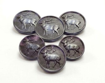 Peut inclure: Un ensemble de six boutons circulaires violet foncé, chacun présentant un relief argenté en forme de cerf debout. Le fond de chaque bouton est orné de fines lignes horizontales, créant un aspect texturé derrière la silhouette du cerf.