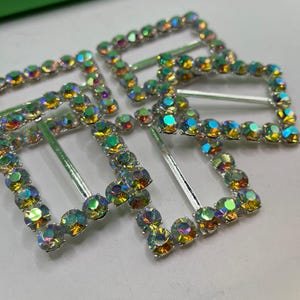 Może przedstawiać: Trzy srebrne spinki do włosów z tęczowymi kryształkami w kształcie prostokąta. Kryształki są ułożone w kształt kwadratu wokół spinki.