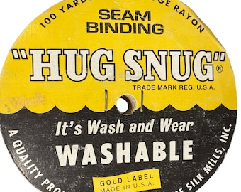 May include: A round yellow and black spool of Hug Snug seam binding. The label reads 100 Yards Woven Edge Rayon, Hug Snug, It's Wash and Wear, Washable, Gold Label Made in U.S.A., and A Quality Product of Lawrence Schiff Silk Mills, Inc.