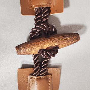 May include: A brown leather toggle with a brown rope and a wooden toggle bar. The toggle is used for fastening clothing.