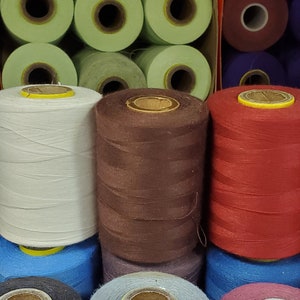 May include: A close-up of a box of thread spools in various colors, including white, brown, red, blue, and purple. The box is labeled "cansew inc. MONTRÉAL, QC, CANADA".