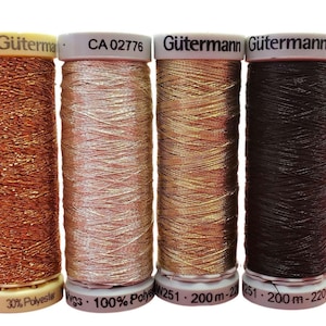 Può includere: Quattro rocchetti di filo metallizzato Gütermann in rame, oro rosa, oro e marrone scuro. I rocchetti hanno etichette bianche con testo nero, tra cui il marchio, i codici prodotto e il contenuto di fibra. Il filo è avvolto su rocchetti di plastica.