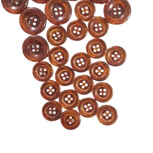 May include: A selection of brown buttons in different sizes, set against a white backdrop. The buttons have a glossy finish and four holes for sewing. Suitable for sewing projects.