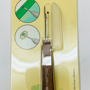 May include: A brown seam ripper with a white plastic cover and a metal blade. The packaging is yellow with green clover leaves and the text "Clover Seam Ripper, Découde-Vite, Descosedor, Nah trennen, Art No. 463, Clover Mfg. Co., Ltd. Japan, Experience the Clover difference."