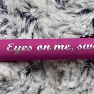 Pu&ograve; includere: Una penna rosa con una clip argentata e una fascia argentata. La penna ha le parole "Eyes on me, sweetheart" incise.