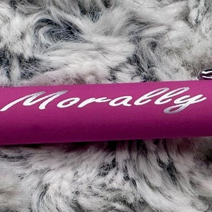 Pu&ograve; includere: Una penna rosa con una clip argentata e una punta argentata. La penna &egrave; incisa con le parole "Morally Gray".
