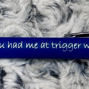 Pu&ograve; includere: Una penna blu con dettagli argentati e l'iscrizione "You had me at trigger warning" sul fusto.