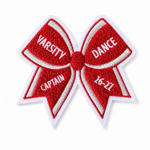 May include: A red and white embroidered bow-shaped patch. The patch features the words "VARSITY CAPTAIN" and "DANCE 16-21" embroidered in white. The bow has a white border and white accents.