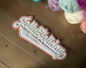 May include: A pink and white felt patch with the text "Fabulous" in a cursive font. The patch is shaped like a baseball.