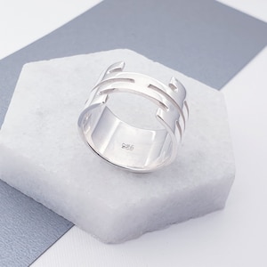 May include: A silver ring with a geometric design. The ring is marked with "925" on the inside.