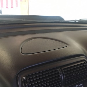 May include: A black car dashboard with a textured surface. The dashboard features an oval-shaped speaker area and air vents. The windshield wipers are visible at the top of the image.