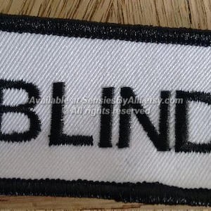 May include: White rectangular patch with black border and the word "BLIND" embroidered in black.