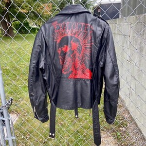 May include: Black leather jacket with a red graphic on the back that says "THE EXPLOITED". The jacket has a classic biker style with a notched collar, asymmetrical zipper, and belt detail at the waist.