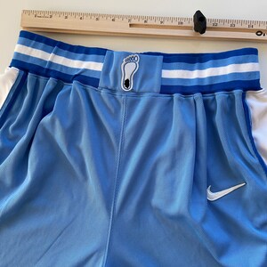 Op de afbeelding: Lichtblauwe basketbalshorts met een witte en blauwe tailleband. De tailleband heeft een klein blauw patch met een wit voetafdruklogo. De shorts hebben een wit Nike swoosh-logo aan de rechterkant.