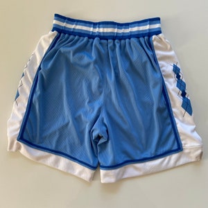 Op de afbeelding: Lichtblauwe basketbalshorts met witte en blauwe bies. De shorts hebben een ruitpatroon aan de zijkanten.