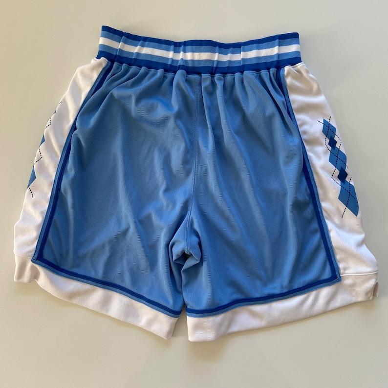Op de afbeelding: Lichtblauwe basketbalshorts met witte en blauwe bies. De shorts hebben een ruitpatroon aan de zijkanten.