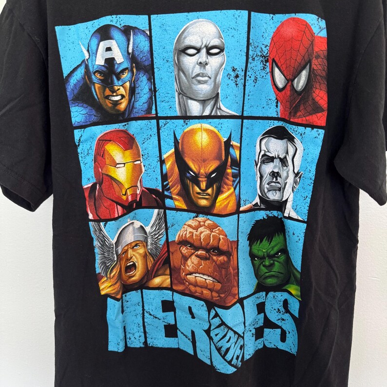 May include: Black t-shirt featuring a grid of Marvel superhero portraits, including Captain America, Spider-Man, and Iron Man. The word "HEROES" is printed in blue, with the Marvel logo below.