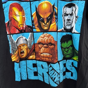 May include: Black t-shirt featuring a grid of Marvel comic book heroes. Iron Man, Wolverine, and Thor are among the characters displayed. The word "HEROES" is printed in large, distressed blue letters across the bottom, with the Marvel logo.