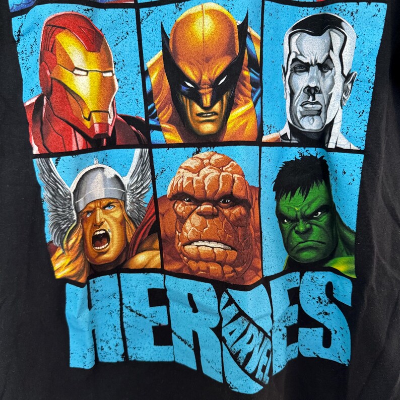 May include: Black t-shirt featuring a grid of Marvel comic book heroes. Iron Man, Wolverine, and Thor are among the characters displayed. The word "HEROES" is printed in large, distressed blue letters across the bottom, with the Marvel logo.
