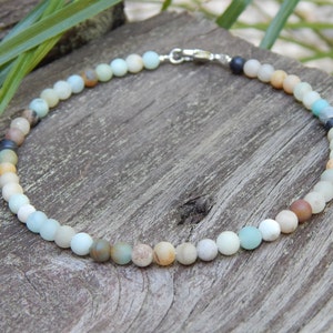May include: A delicate necklace made of small, round, multi-colored beads. The beads are a mix of light blue, green, brown, and white. The necklace is strung on a silver chain.