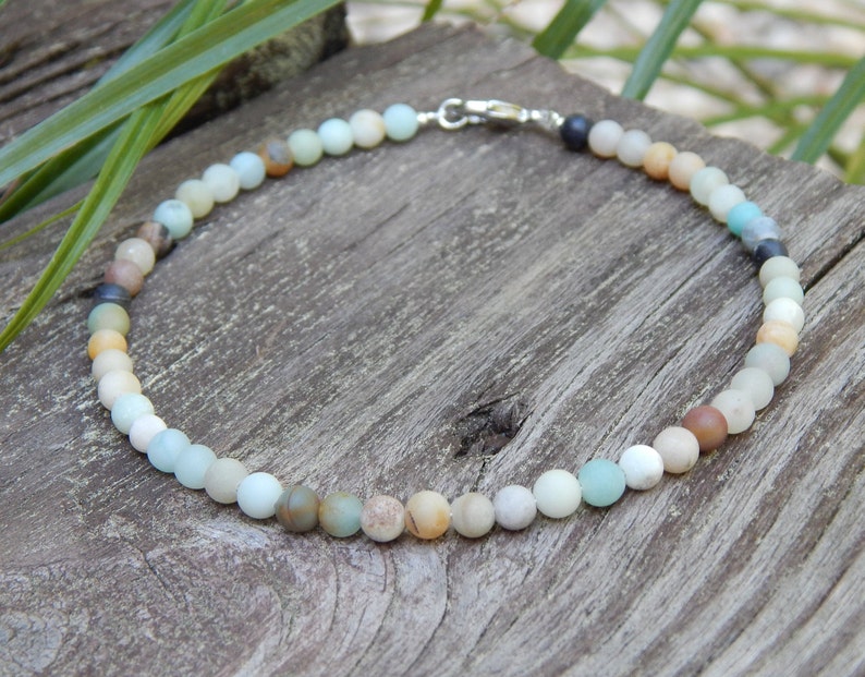 May include: A delicate necklace made of small, round, multi-colored beads. The beads are a mix of light blue, green, brown, and white. The necklace is strung on a silver chain.