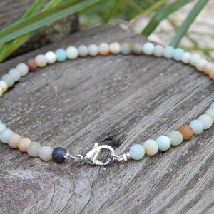 May include: A multi-colored beaded bracelet with a silver clasp. The beads are various shades of green, brown, and white.