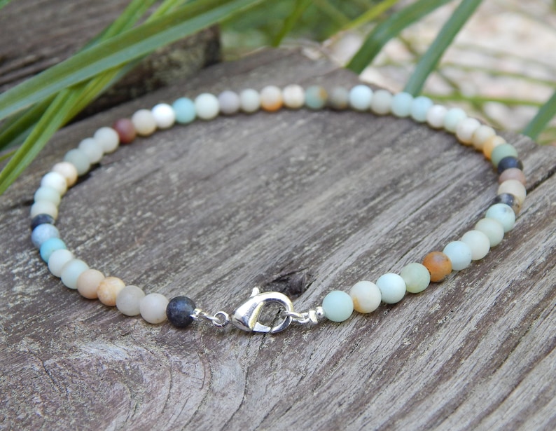 May include: A multi-colored beaded bracelet with a silver clasp. The beads are various shades of green, brown, and white.