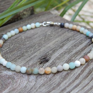 May include: A necklace made of various shades of green, brown, and white beads. The beads are round and have a smooth, polished finish. The necklace is strung on a silver chain.