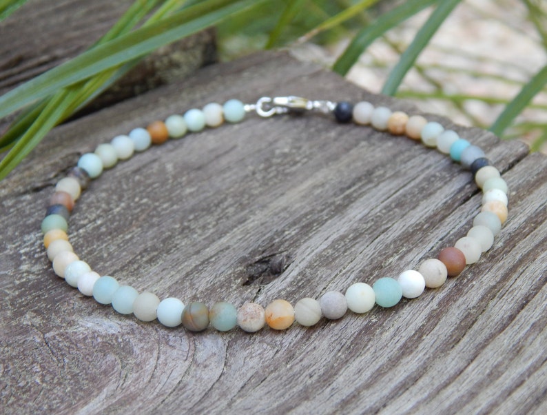 May include: A necklace made of various shades of green, brown, and white beads. The beads are round and have a smooth, polished finish. The necklace is strung on a silver chain.
