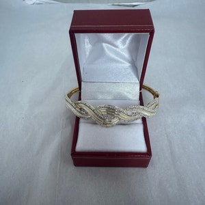 May include: A gold and silver bangle bracelet with a wavy design set with small clear stones. The bracelet is in a red velvet box.
