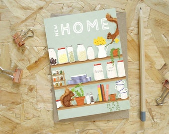Puede incluir: Tarjeta de felicitación con la frase "NEW HOME" y una ilustración de una estantería de cocina con tarros, plantas y una ardilla. La tarjeta está sobre una superficie de madera, con un lápiz y clips.