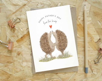 Puede incluir: Tarjeta del Día del Padre con una ilustración en acuarela de dos erizos abrazándose, con el texto "Happy Father's Day from the bump" y un pequeño corazón rojo. La tarjeta está sobre un sobre de papel kraft.