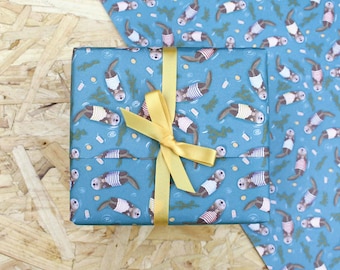 Puede incluir: Un regalo envuelto con papel de regalo azul con un estampado de nutrias nadando en el agua, con camisas a rayas. El regalo está atado con una cinta amarilla. Se ve papel de regalo adicional con el mismo patrón.