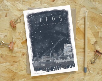 Puede incluir: Una impresión artística en escala de grises del horizonte de Leeds bajo un cielo estrellado. La impresión presenta la palabra "LEEDS" y el texto "THE NORTH OUR CITY". La impresión está sobre papel marrón con un lápiz y clips.