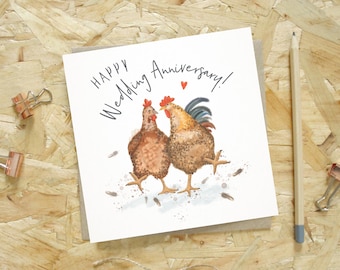 Puede incluir: Tarjeta cuadrada de aniversario de bodas con una ilustración de una gallina y un gallo, con el texto "Happy Wedding Anniversary!". Sobre un fondo de madera clara, con un lápiz y clips.