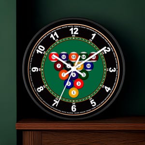 May include: A round black wall clock featuring a green pool table design with billiard balls. The clock face displays numbers and text around the edge, with white hands indicating the time. A decorative piece for game rooms.