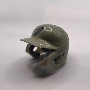 Puede incluir: Un casco de bateo de béisbol verde con una máscara facial negra y un logotipo blanco en el lateral.