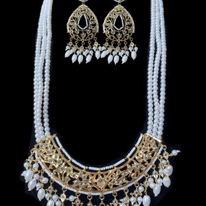 May include: A white pearl necklace with a gold pendant and matching earrings. The pendant is a large, ornate design with intricate details. The earrings are smaller versions of the pendant.