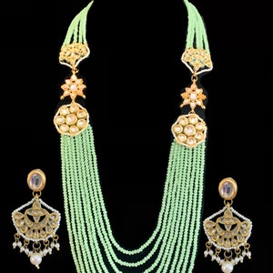May include: A multi-strand necklace with light green beads and gold accents. The necklace has a large, ornate pendant with a floral design and a smaller pendant with a similar design. The necklace is paired with matching earrings with similar designs.