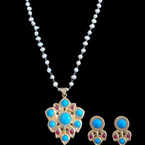 Pode incluir: Um colar de ouro com um pingente de turquesa e pedra vermelha e brincos combinando. O colar é feito de pérolas brancas.