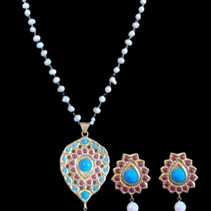 Pode incluir: Um colar de ouro com um pingente turquesa e vermelho e brincos combinando. O colar é feito de pérolas e o pingente tem a forma de uma lágrima com uma pedra turquesa no centro. Os brincos também têm a forma de uma lágrima com pedras turquesas no centro.