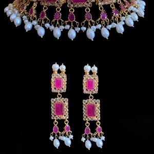 Puede incluir: Un collar gargantilla de oro con piedras preciosas rosas y detalles de perlas blancas. Pendientes a juego con piedras preciosas rosas y perlas blancas.